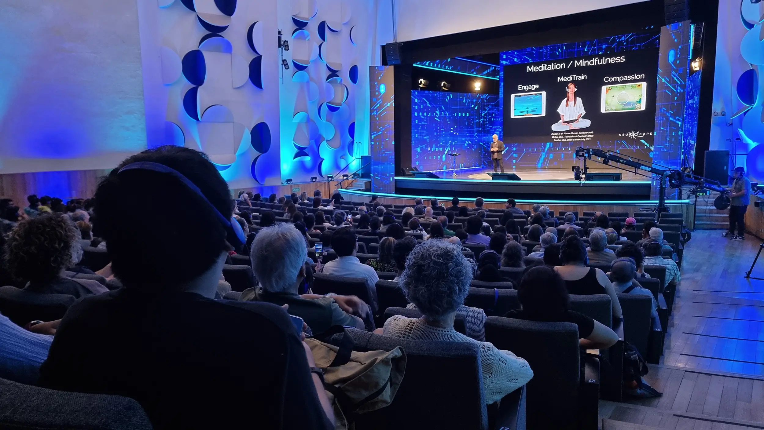 Auditorio de congreso con pantalla y escenario iluminado en azul